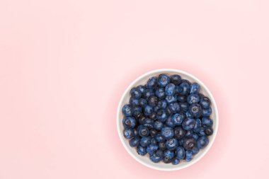 Bir kasede yaban mersini. Renkli bir arka planda yabanmersini. Yazmak için bir yer. Yukarıdan bak. Pasuda serpiştirin. Doğal meyveler. Taze olgun yaban mersininin kabın içindeki en üst görüntüsü.