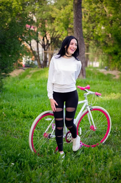 Menina em uma bicicleta vermelha e branca. Um muito jovem sexy bronzeado atletismo menina passeios na natureza. morena alegre e sorridente. bons números . — Fotografia de Stock