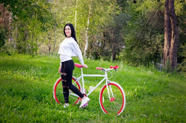 Menina em uma bicicleta vermelha e branca. Um muito jovem sexy bronzeado atletismo menina passeios na natureza. morena alegre e sorridente. bons números . — Fotografia de Stock