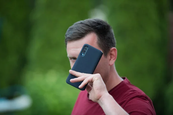 A man holds a phone in a protective case. phone safety from falling. bumper on the phone. dark phone. place to write. Smartphone on blurred park background in black plastic case back view. Smartphone