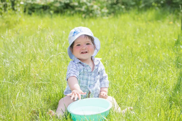 Enfant joue avec un bassin d'eau sur l'herbe. Bébé garçon drôle jouant dehors avec de l'eau et des bulles. Un petit garçon mignon fait un drôle de visage alors qu'il joue dehors avec du savon à bulles et de l'eau dans un t de lavage — Photo