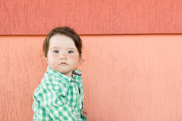 Baby op een koraalachtergrond. Kleine jongen. in een geruit groen en wit shirt. — Stockfoto