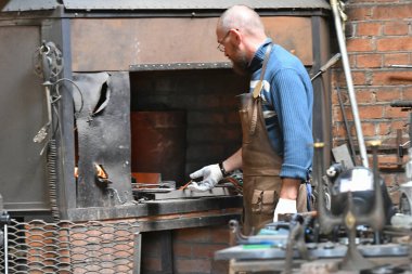 Demirci ocakta demir ısıtır. Demirci, atölyede kızgın demir döşeyen havai fişeklerle nalbantta alevler yakıyor.