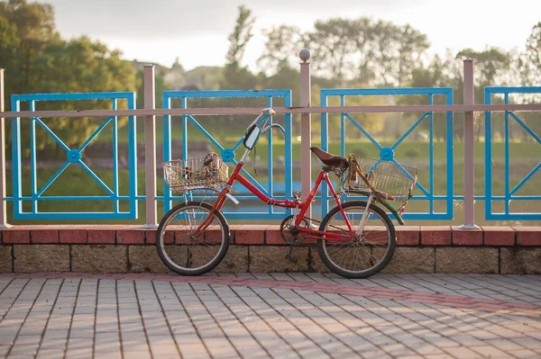 Altes rotes Fahrrad mit Körben steht bei Sonnenuntergang am Zaun — Stockfoto