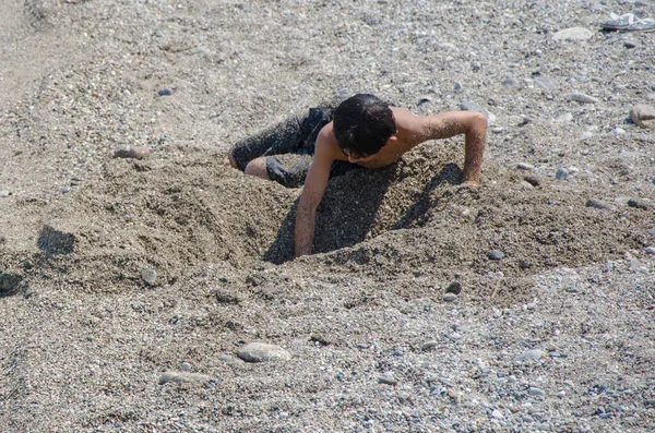 Un garçon joue sur la plage avec du sable sous le soleil brûlant — Photo