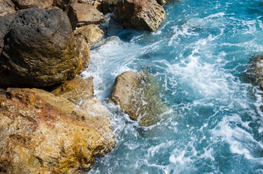 Mavi dalgalar kıyıdaki kayalarda kırılır.
