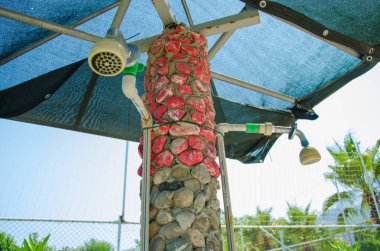 Kırmızı taş sokağında, kumsalın yanındaki mavi şemsiyenin altında duş al.