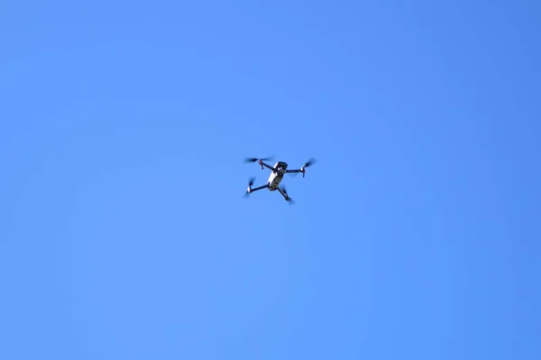 Latający quadcopter na niebie. Czworonożny dron lecący na niebieskim niebie. Biały mały dron lecący na niebieskim niebie — Zdjęcie stockowe