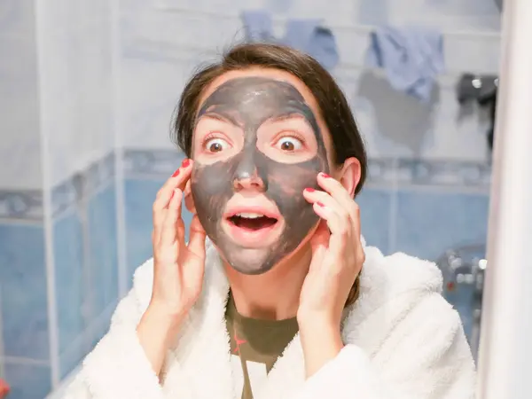 戴面具的女孩在镜子旁边吃惊极了。 皮肤护理。 利兹皮肤面具的惊人效果. — 图库照片