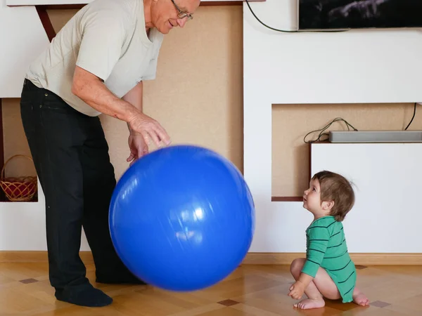 The child plays with the grandfather a ball. play a big blue ball at home. A boy is playing with his grandfather. — ストック写真