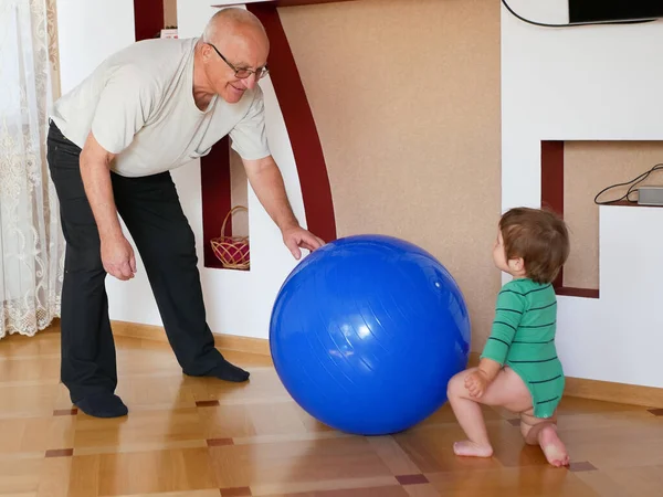 Spielt das Kind mit dem Großvater den Ball. zu Hause einen großen blauen Ball spielen. ein Junge spielt mit seinem Großvater. — Stockfoto