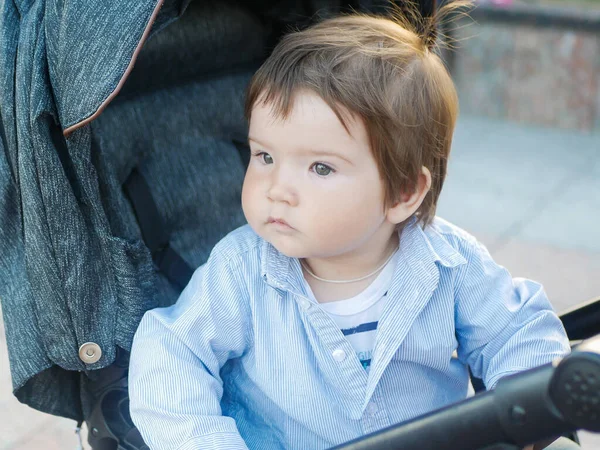 Bebê sentado em um carrinho cinza. segurando um brinquedo nas mãos. Um passeio quente para o bebê . — Fotografia de Stock