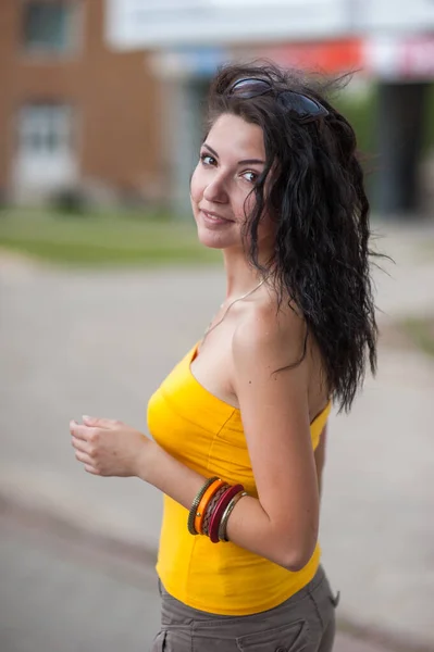 A young girl walks through the city. bracelets in a yellow t-shirt. Closeup portrait of a self-confident free amazing lady, she walks around the city, stylish accessories, long dark hair, makeup, urba — Stock Photo, Image