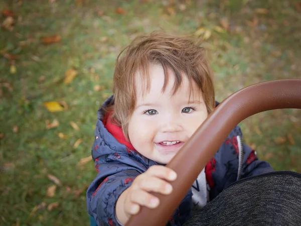 Kind mit Kinderwagen, das in die Kamera blickt. Glückliches Baby hält einen Kinderwagen. Natur im Hintergrund — Stockfoto