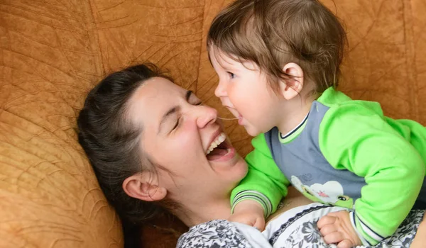Baby bites moms nose. Happy mother with baby. A boy bites his mothers nose on the couch. having fun with your beloved mother — Stock Photo, Image