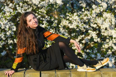 Beyaz çiçekli bir ağacın arka planındaki kız. Uzun saçlı, saman şapkalı, klasik bluzlu, mavi küpeli, çiçek açan aparatta poz veren zarif bir hanımın açık hava portresi.