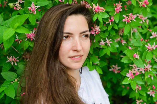 Joven chica hermosa cerca de las flores. Fotón verde y flores. Retrato de una joven hermosa chica cerca de las flores. Retrato de una joven hermosa mujer, cara bonita de cerca, grandes labios rosados, pelo liso dr — Foto de Stock