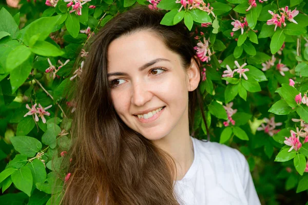 Joven chica hermosa cerca de las flores. Fotón verde y flores. Retrato de una joven hermosa chica cerca de las flores. Retrato de una joven hermosa mujer, cara bonita de cerca, grandes labios rosados, pelo liso dr — Foto de Stock