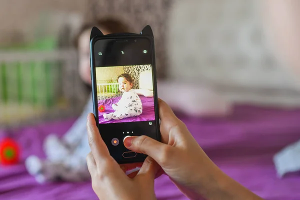 Mom photographs the baby on the phone. close on the phone. mom photographed her little son-girl using a device-oriented smartphone