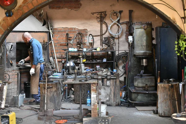 An experienced blacksmith works with open fire. A blacksmith extinguishes a flame in a forge with a spark firework, forges hot iron in a workshop — Stock Photo, Image