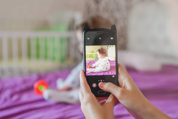 Мама фотографирует своего ребенка по телефону. Мама фотографирует своего новорожденного ребенка на смартфоне. Семейные воспоминания . — стоковое фото
