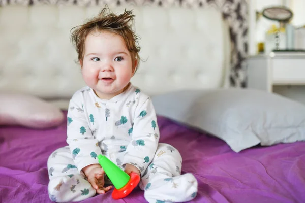 Baby poseert op camera zittend op het bed. Het kind speelt in het beddengoed. — Stockfoto