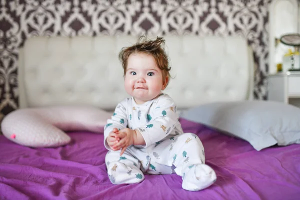 Retrato de un niño pequeño sentado en la cama. Retrato de un bebé sentado en la cama. Retrato de un niño pequeño sentado en una cama, mirando recto, una ceja levantada — Foto de Stock