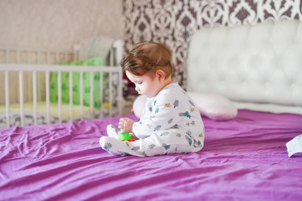 Ребенок играет с игрушками на кровати. Мальчик кусает игрушку на кровати дома — стоковое фото