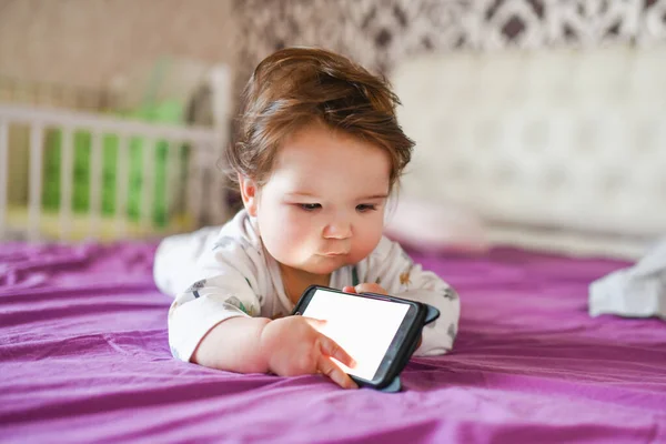 Вред от мобильного устройства ребенку. Малыш Тоддлер лежит, глядя на телефон. Концепция зависимости от гаджетов — стоковое фото