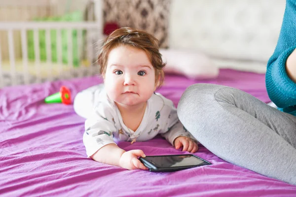 Малыш с телефоном. на кровати. знание мобильных устройств. Малыш с мобильным телефоном. Маленький ребенок в разноцветной полосатой одежде с мобильным телефоном — стоковое фото