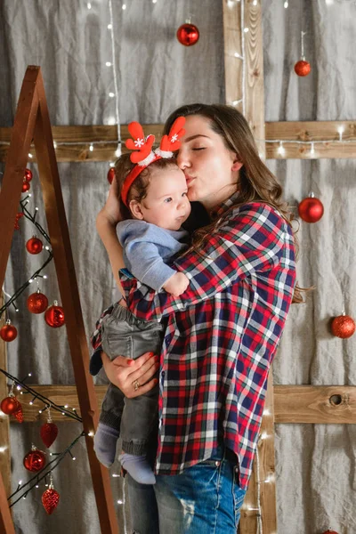 Noel geçmişinde çocuklu bir anne. Küçük bir çocuğun kafasında kırmızı boynuzlar. Yeni yıl. Noel kutlaması — Stok fotoğraf