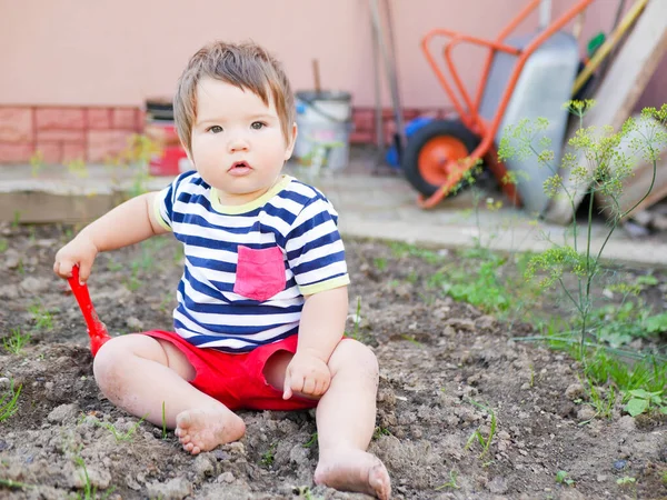 一个男孩在街上玩铲子。 男婴和红色铲子 0-1岁男孩 — 图库照片