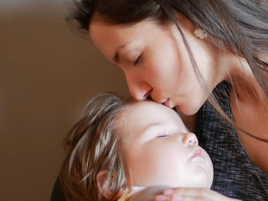 Annem uyuyan bir bebeği kollarında tutuyor ve onu alnından öpüyor. Kollarında bebek olan bir kadın. Kız çocuğu öpüyor..