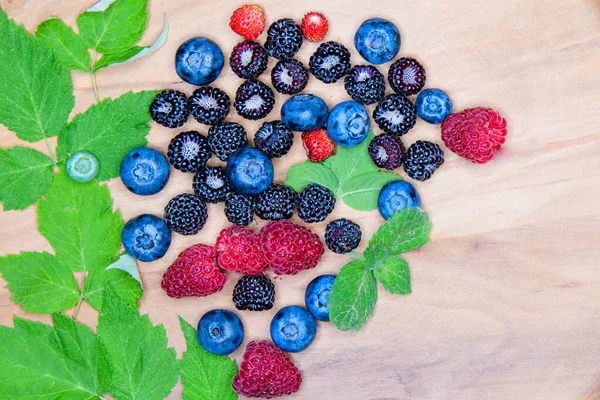 Wild berries on a wooden plate. Composition of three types of summer berries lying on a textured wooden plate. Top view on a wooden plate filled with many berries.