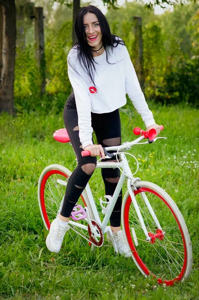 Meisje op een rood-witte fiets. Een mooi jong sexy gebruind atletisch meisje rijdt in de natuur. Vrolijk en lachend brunette. goede cijfers. — Stockfoto