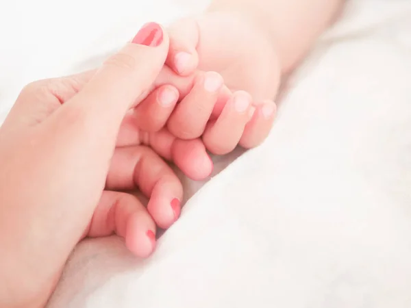 Mom holds the hand of a newborn baby. Close-up. A place to write. Placing text. defocusing. Baby's hand holding finger to mom. — Stock Photo, Image