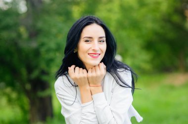 Doğada neşeli bir kızın portresi. Siyah saçlı, beyaz tişörtlü, boyalı başlıklı. Doğal duygular. Gözleri açık, gülümseyen güzel kız..