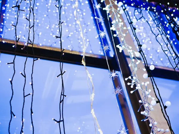Οι γιρλάντες κρέμονται στο παράθυρο. πολύχρωμες γιρλάντες λαμπτήρων σε ένα κοντινό παράθυρο. Πρωτοχρονιάτικη γιρλάντα — Φωτογραφία Αρχείου