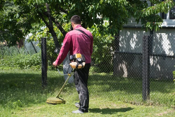 한 남자가 잔디 깎는 기계에 잔디를 깍는다. 바지 및 도구. — 스톡 사진