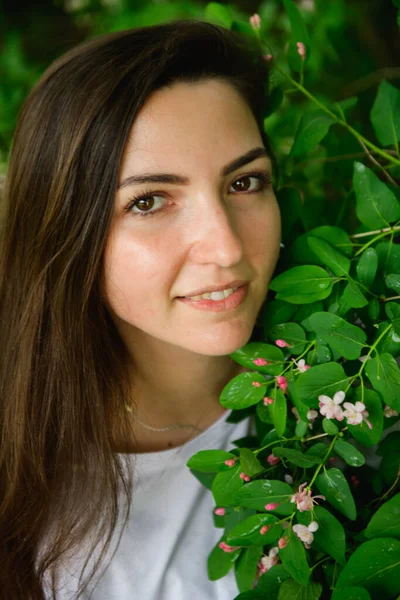 Young beautiful girl near the flowers. photon green and flowers. Portrait of young beautiful girl near flowers. Portrait of young beautiful woman, pretty face close-up, big pink lips, straight hair dr