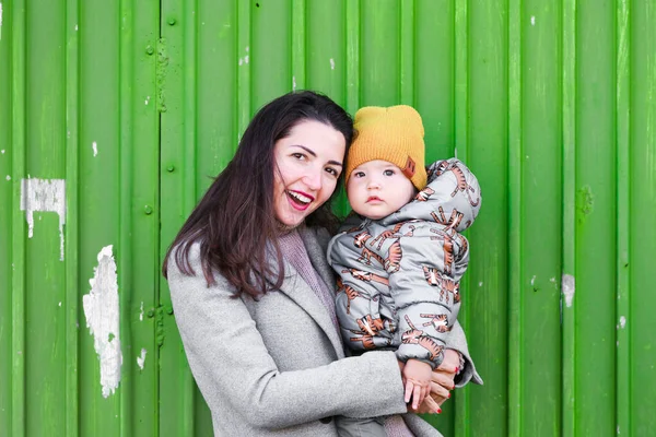 mom with a baby on a green background. wear a hat and coat. place to record. dressed in a cold pagoda. clothes and style. natural emotions. family, motherhood, parenting, people and childcare concept