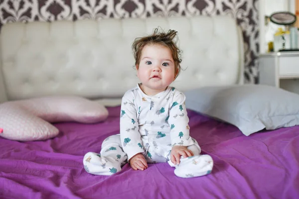 Portret van een klein kind zittend op het bed. Portret van een kleine baby die op het bed zit. Portret van een klein kind zittend op een bed, recht kijkend, een wenkbrauw opgeheven — Stockfoto