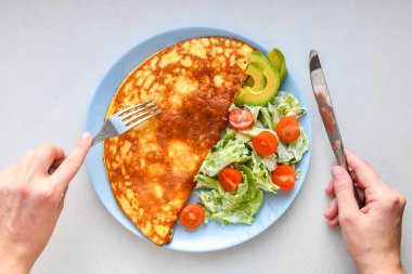 sebze ile kızarmış yumurta. çerçeveiçinde eller. Beyaz bir masa üzerinde mavi bir tabak üzerinde sebze omlet, üst görünümü