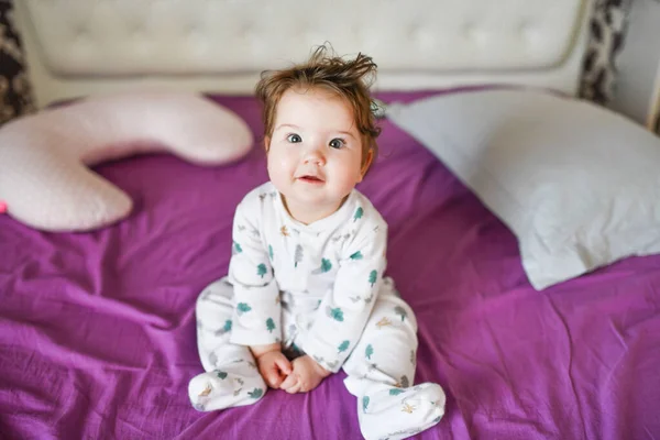 De baby zit op het bed. Leuk meisje op het bed in de slaapkamer — Stockfoto