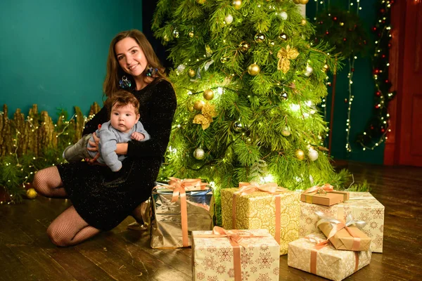 Noel ağacında anne ve bebek kucaklaması. Mutlu bebek ve annesi çerçeveye bakıyorlar. Noel'de oğluyla birlikte anne kucaklıyor. ve eğlenin. yeni yıl için yenidoğan bebek. — Stok fotoğraf