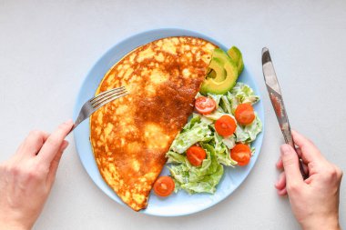 sebze ile kızarmış yumurta. çerçeveiçinde eller. Beyaz bir masa üzerinde mavi bir tabak üzerinde sebze omlet, üst görünümü