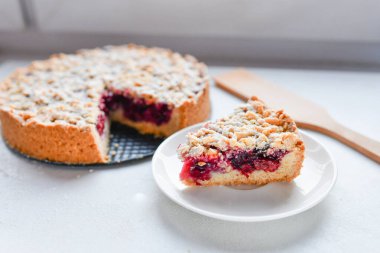 Böğürtlenli. Bir dilim ev yapımı vişneli turta tabakta ve bütün turta dilimlenmiş fırın tabağında peçete üzerinde ahşap masa, klasik tarif, yukarıdan görüş. 