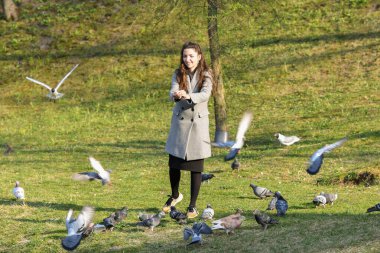 Kız güneşli havada kuşları besler. Güneşli sonbahar gününde parkta kuşları besleyen güzel bir kadın. 