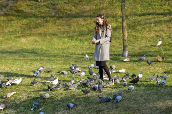 Chica alimenta a los pájaros en tiempo soleado. Hermosa mujer joven alimentando aves en el parque en el soleado día de otoño —  Fotos de Stock