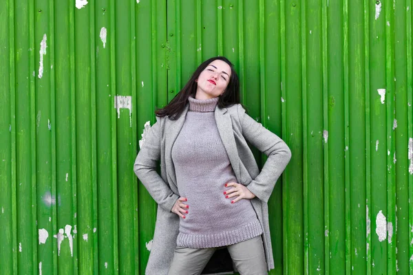 Meisje op een groene achtergrond. Draag een hoed en jas. plaats om op te nemen. gekleed in een koude pagode. kleren en stijl. natuurlijke emoties. Portret van jonge vrouw tegen een groene achtergrond — Stockfoto